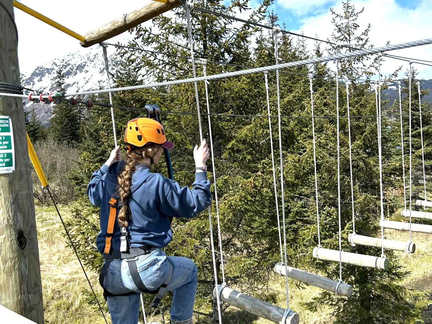 Person in helmet navigating a high ropes course with a forest background.