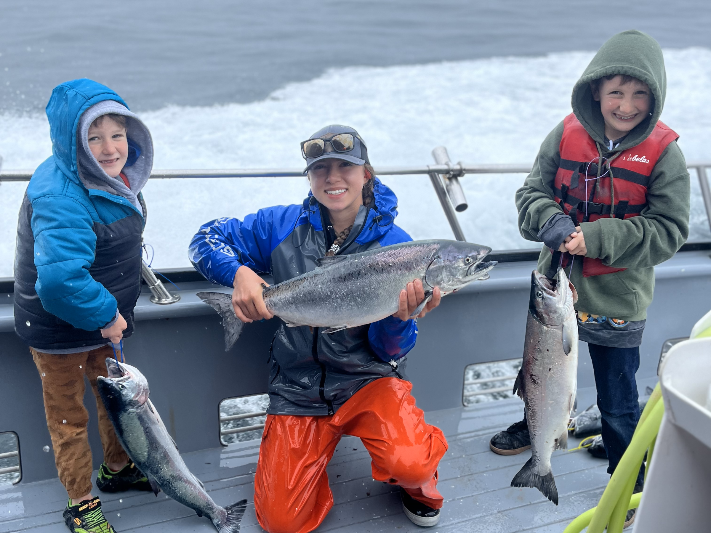 Three people on a boat holding large fish, with ocean in the background.