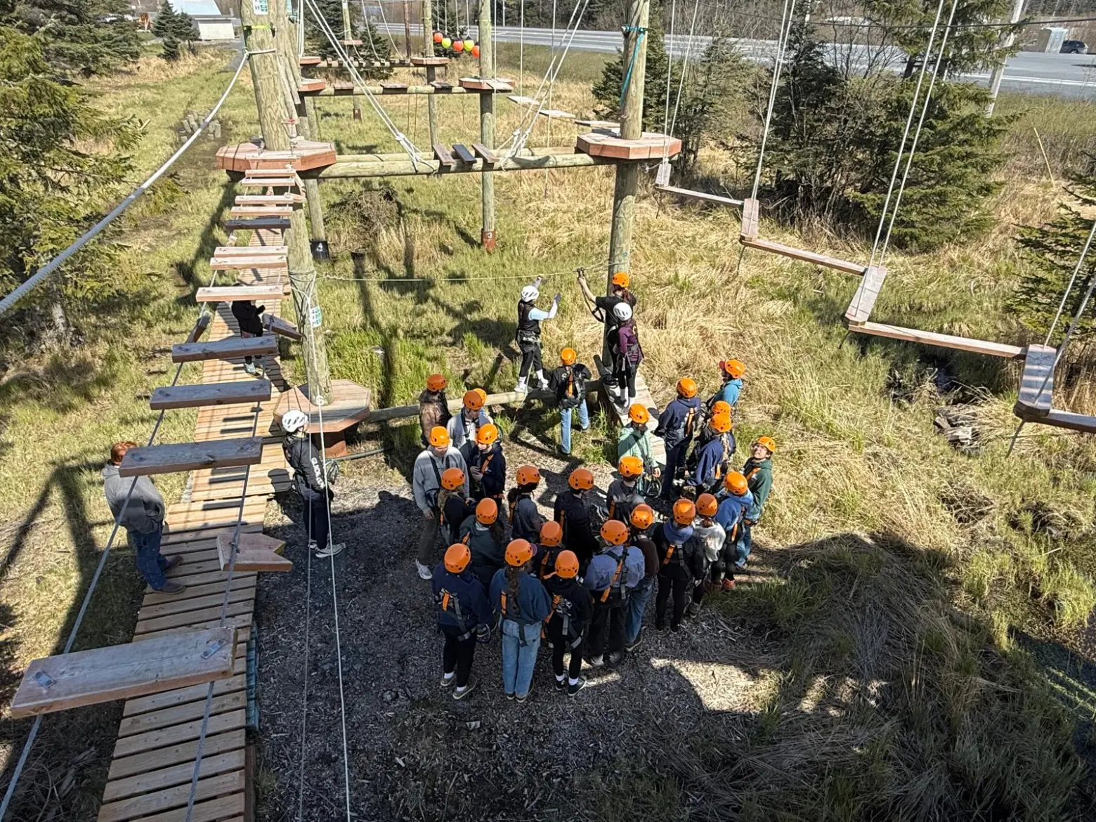 Group of people in helmets at a ropes course surrounded by trees and wooden platforms.