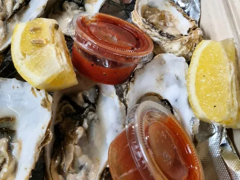 Opened oysters with lemon wedges and two sauce containers on foil.