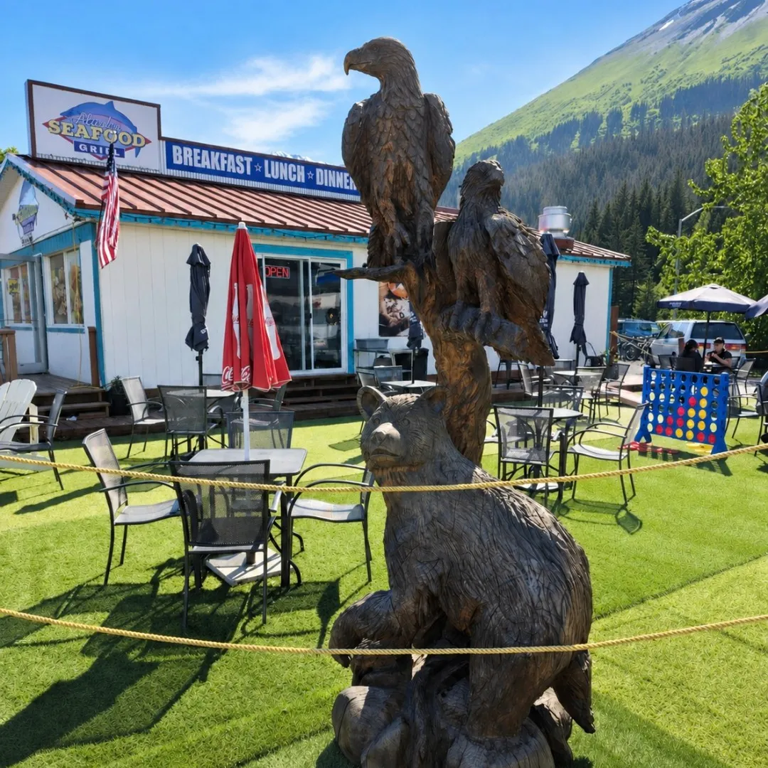 Wooden animal sculptures in outdoor restaurant seating area on artificial grass.