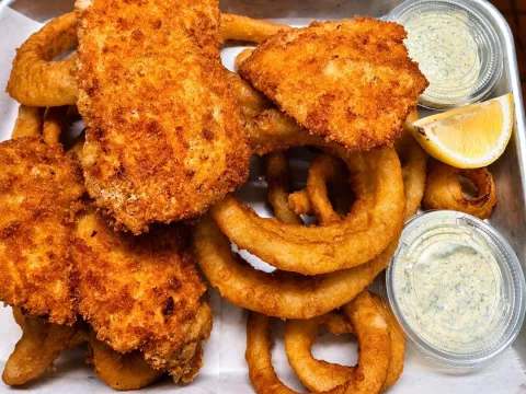 Fried fish fillets and onion rings with tartar sauce and lemon wedge on a tray.