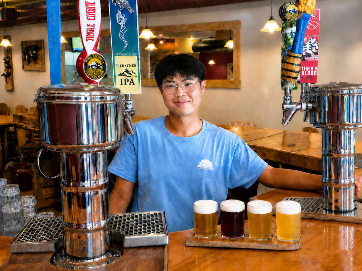 Man in a blue shirt stands behind a bar with three beer taps and four beer glasses in front.