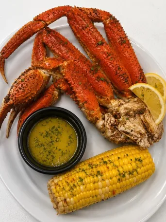 Crab legs with garlic butter, corn, and lemon wedges on a white plate.