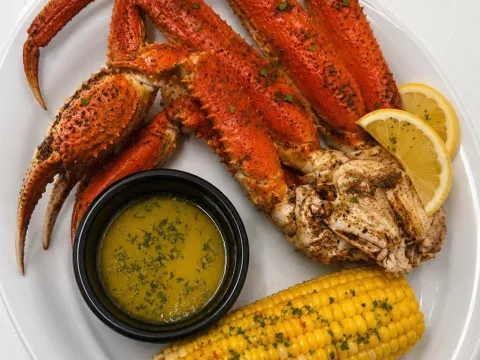 Crab legs with garlic butter, corn, and lemon wedges on a white plate.
