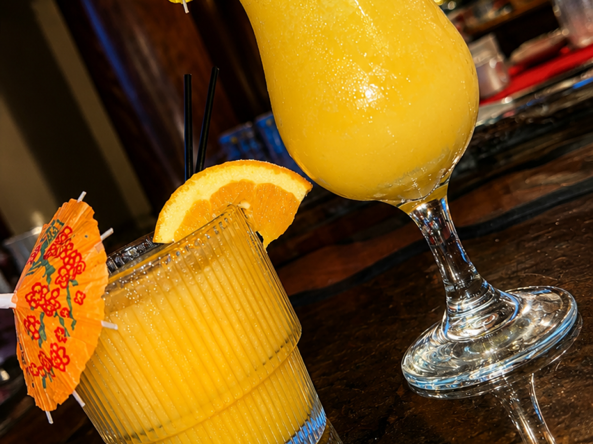 Two tropical cocktails with umbrellas on a bar table.