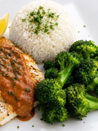 Grilled fish with sauce, broccoli, and rice on a white plate.