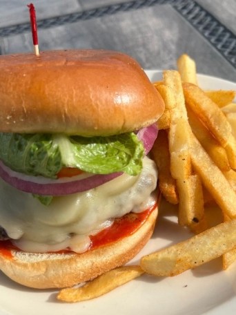 Burger with lettuce, onion, cheese on a bun, served with fries on a white plate.