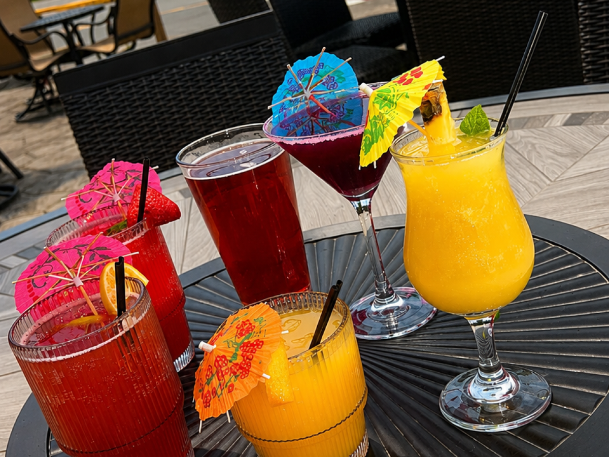 Tray of colorful drinks with umbrellas on an outdoor table.