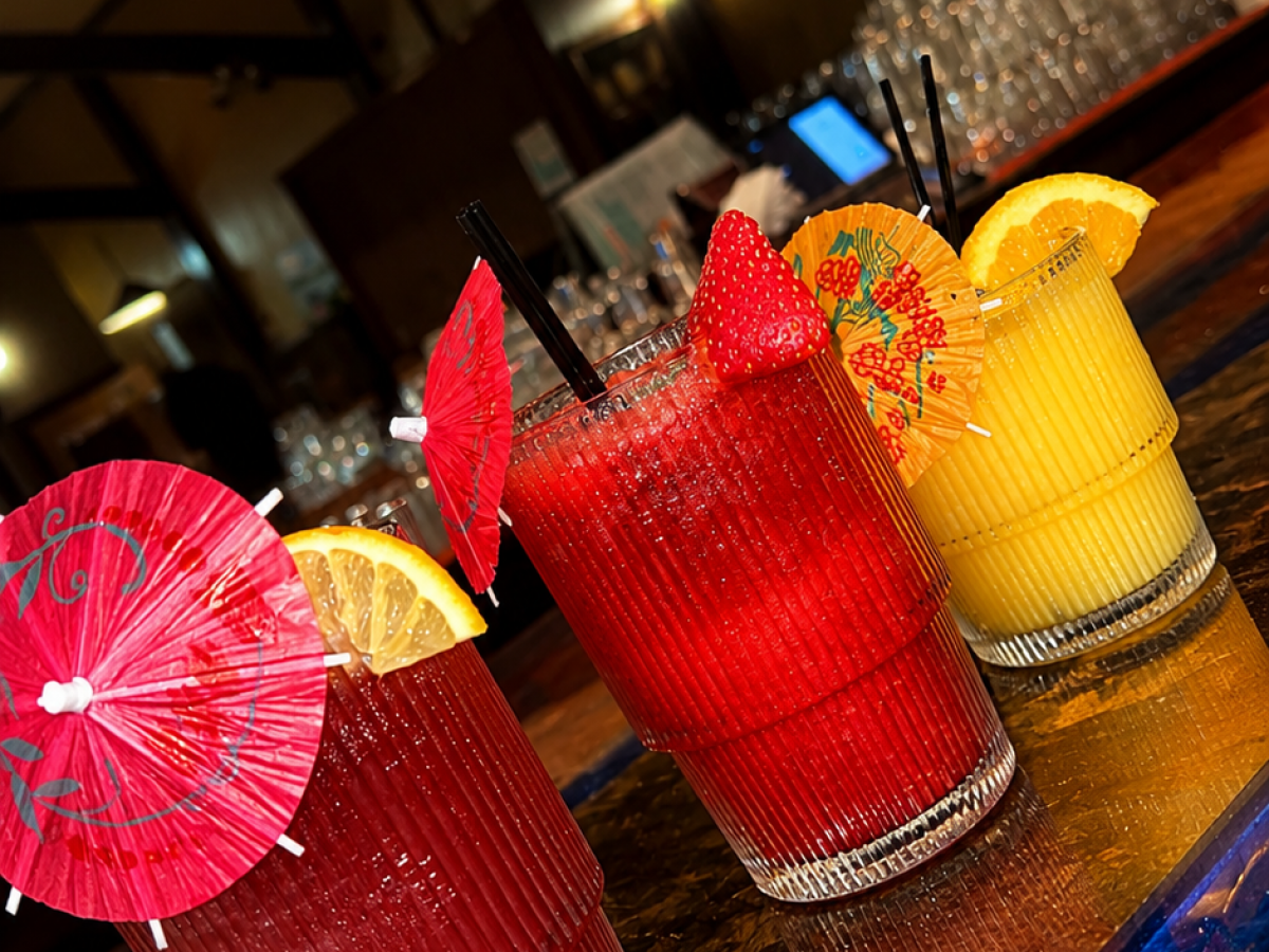 Three colorful cocktails on a bar with fruit garnishes and umbrellas.