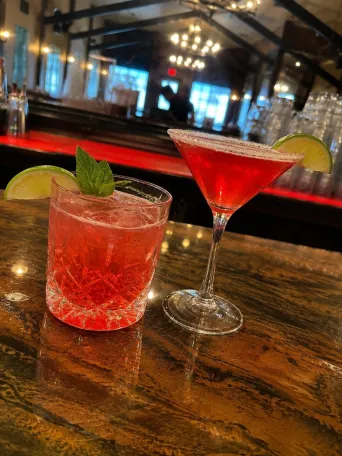 Two cocktails on a bar with a dimly lit background.