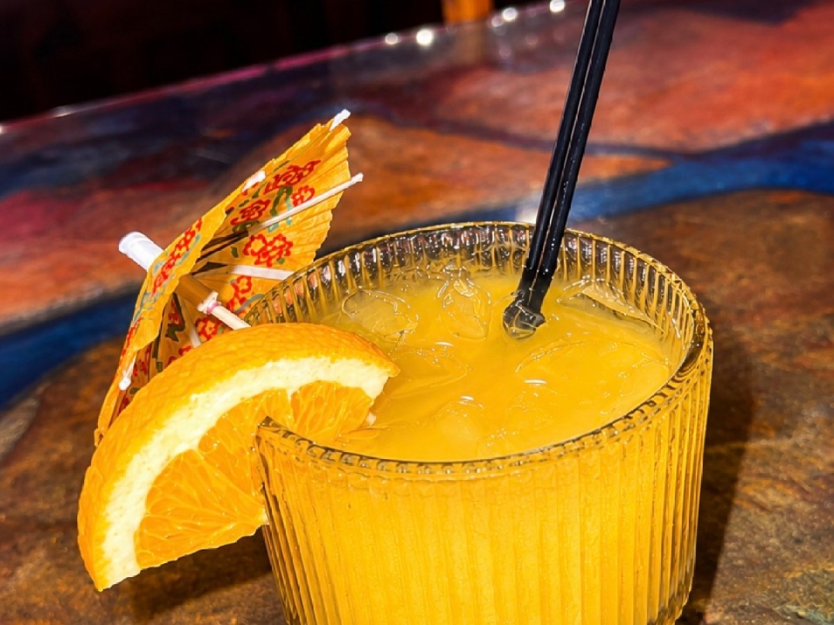 Glass of orange juice with an orange slice and umbrella on a bar.