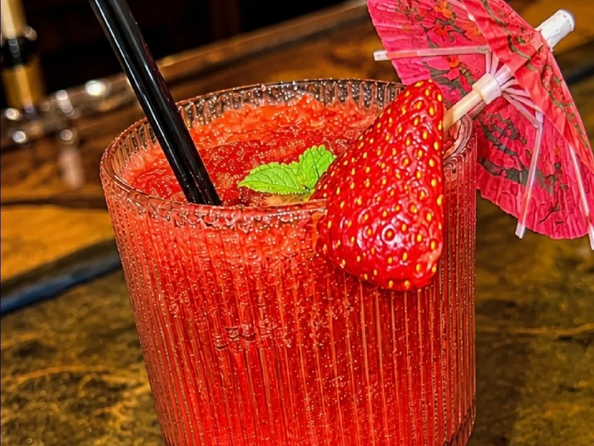 Red frozen drink with straw, umbrella, and strawberry garnish on a bar top.