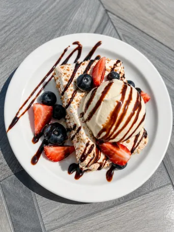 Dessert with ice cream, berries, and chocolate drizzle on a white plate.